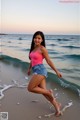 A woman in a pink tank top and denim shorts on the beach.