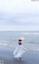 A woman walking on the beach with a hat on.