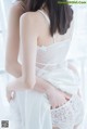 A woman in a white lingerie sitting on a window sill.