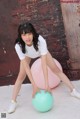 A woman in a white shirt and white sneakers is posing with a pink ball.