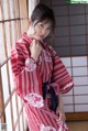 A woman in a red and white kimono leaning against a window.