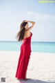 A woman in a red dress standing on a beach.