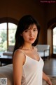 A woman in a white tank top sitting on a bed.