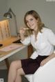 A woman sitting at a desk with a pen in her mouth.